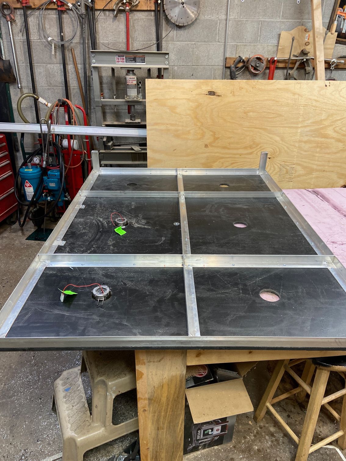 Aluminum-framed table with black inserts on a workbench in a workshop.  Tool storage, equipment and wood in the background.