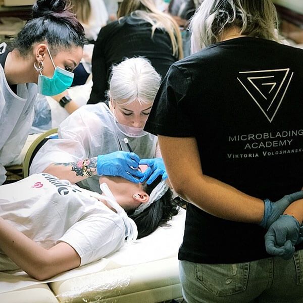 Sessione di formazione sul microblading con una cliente su un lettino da trattamento e due operatori che lavorano a stretto contatto.