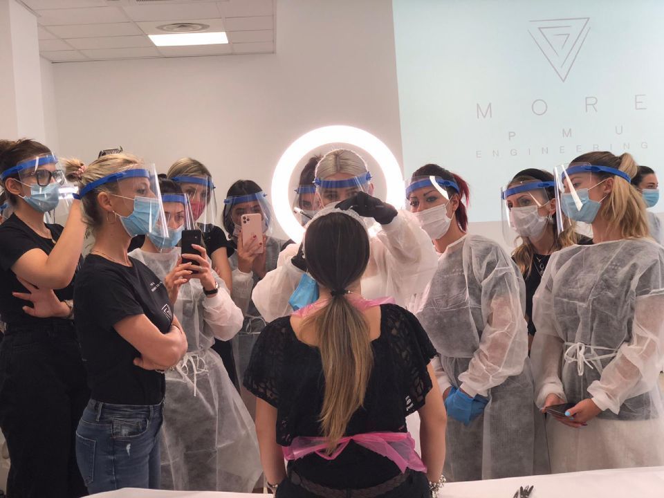 Un gruppo di persone mascherate si è riunito attorno a una persona con una visiera protettiva, in ascolto in un luminoso salone o laboratorio.