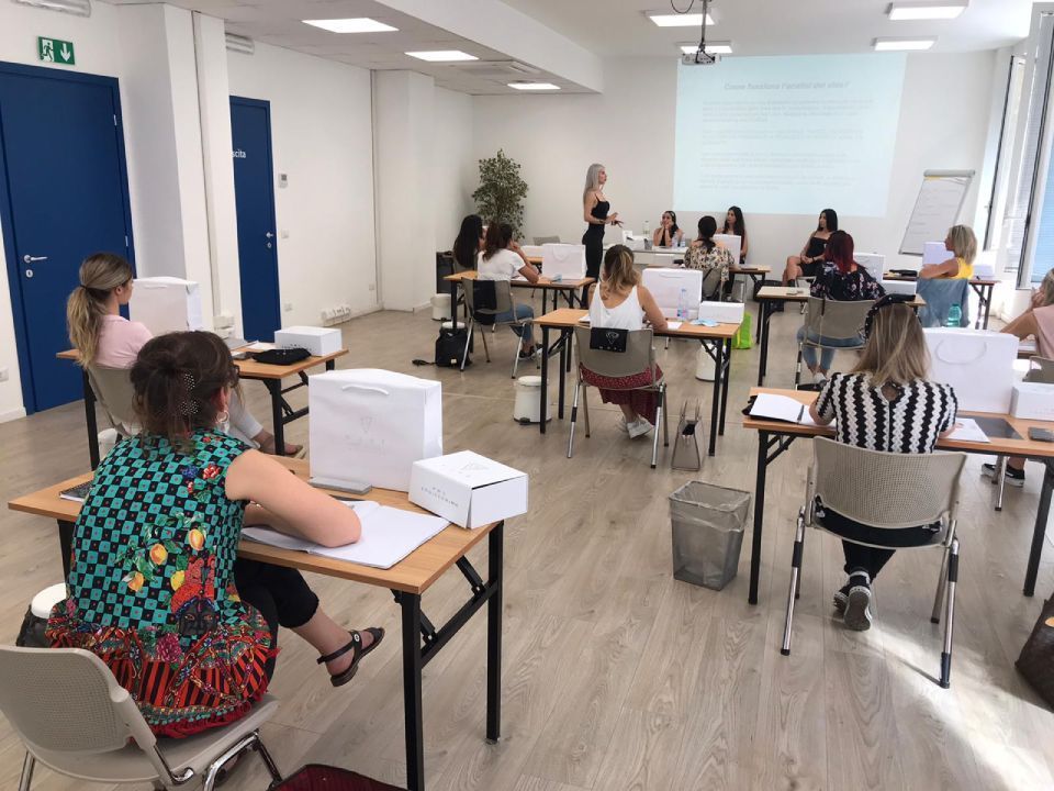 Persone sedute ai banchi in un'aula luminosa durante una lezione di gruppo.