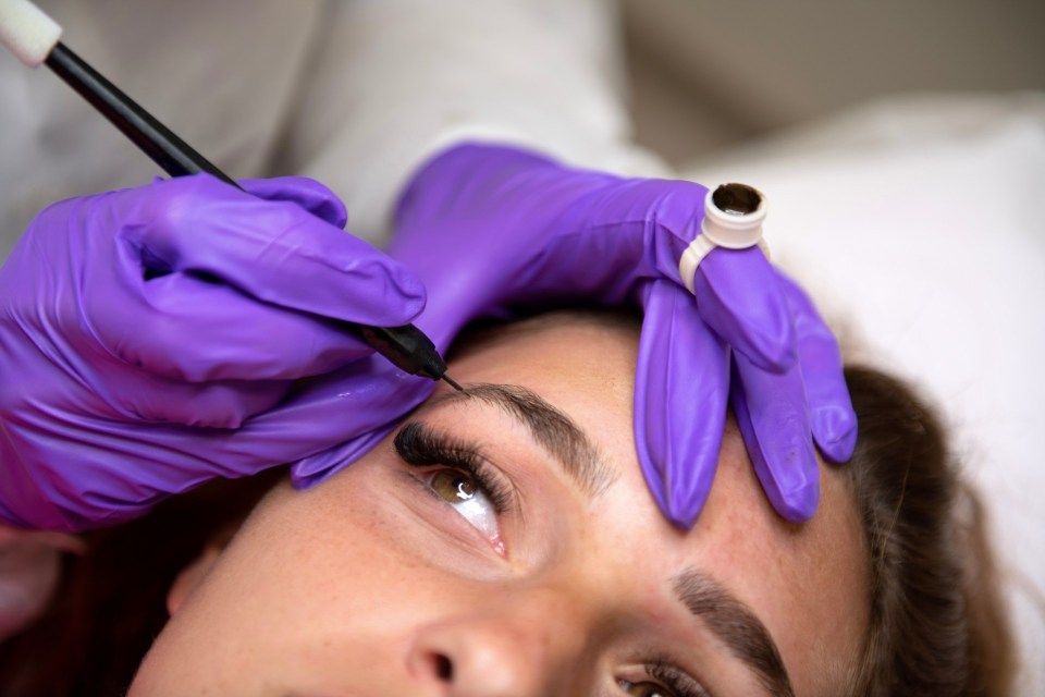 Un'artista con i guanti applica l'eyeliner permanente sull'occhio di una cliente utilizzando uno strumento simile a una penna.