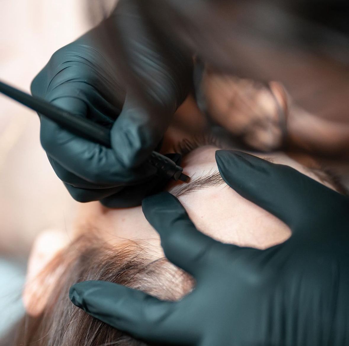 Mani guantate che applicano il trucco alle sopracciglia di una cliente con pennello e matita.