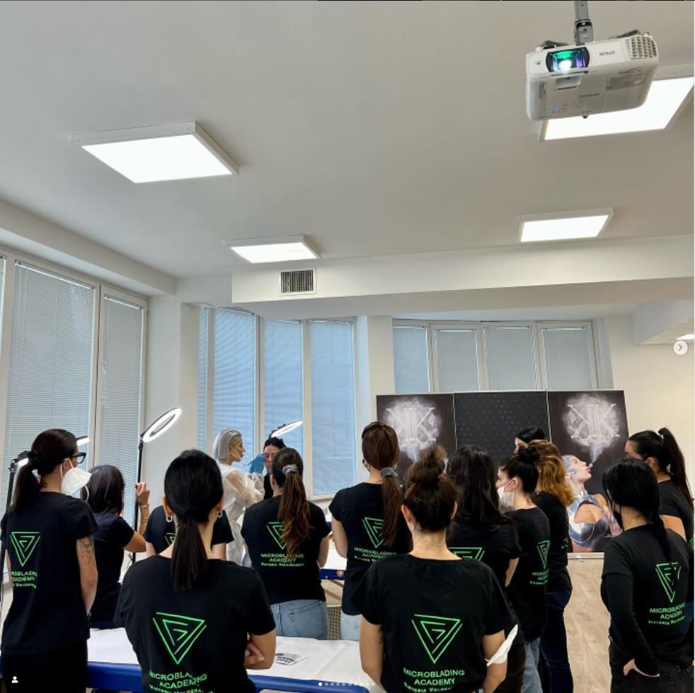 Un gruppo di persone con indosso magliette nere identiche si è riunito in una stanza luminosa, di fronte a una lavagna e a uno schermo per proiezioni.
