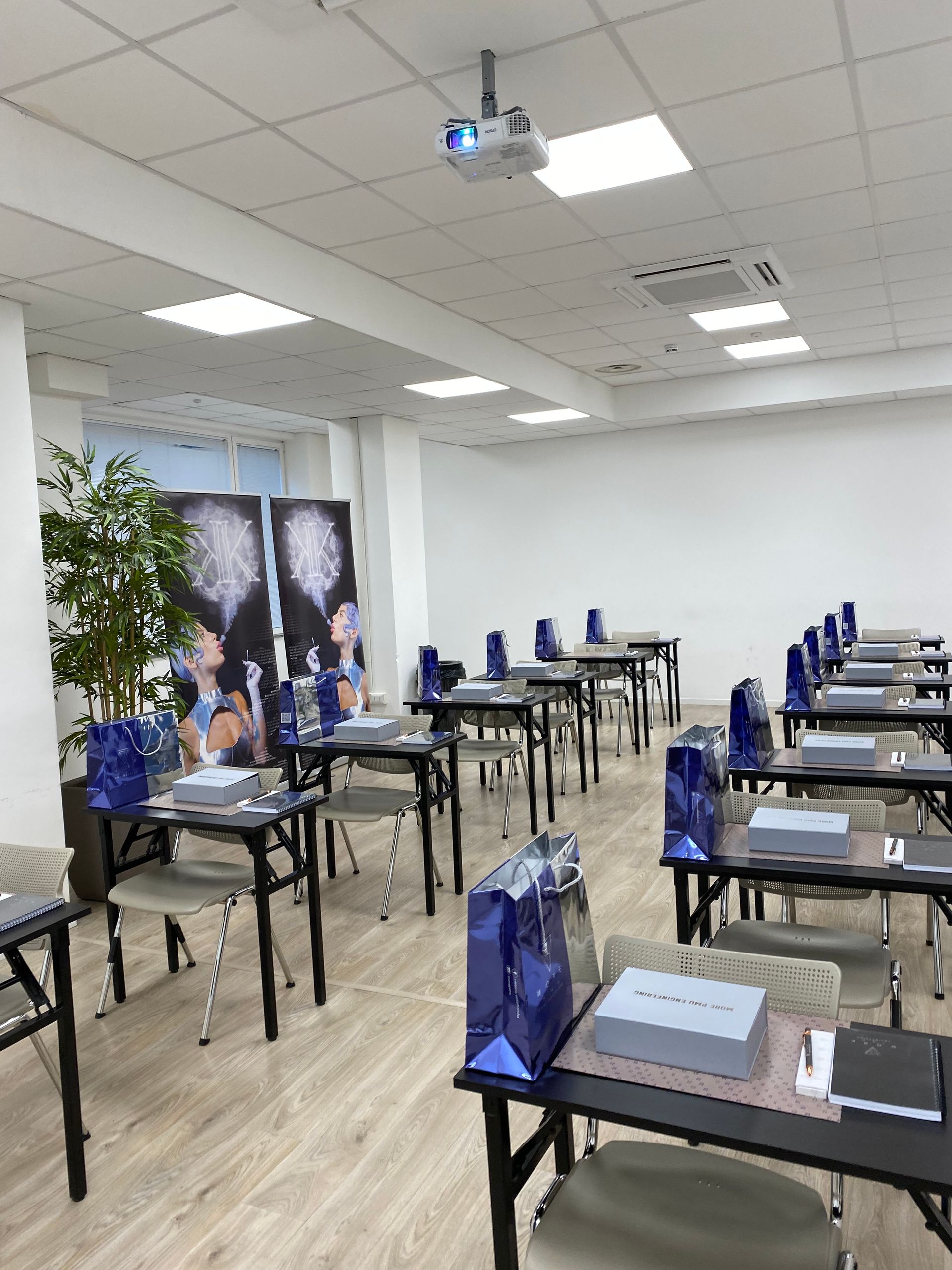 Aula vuota con file di banchi e sacchetti regalo blu su ogni banco, proiettore sopra la testa
