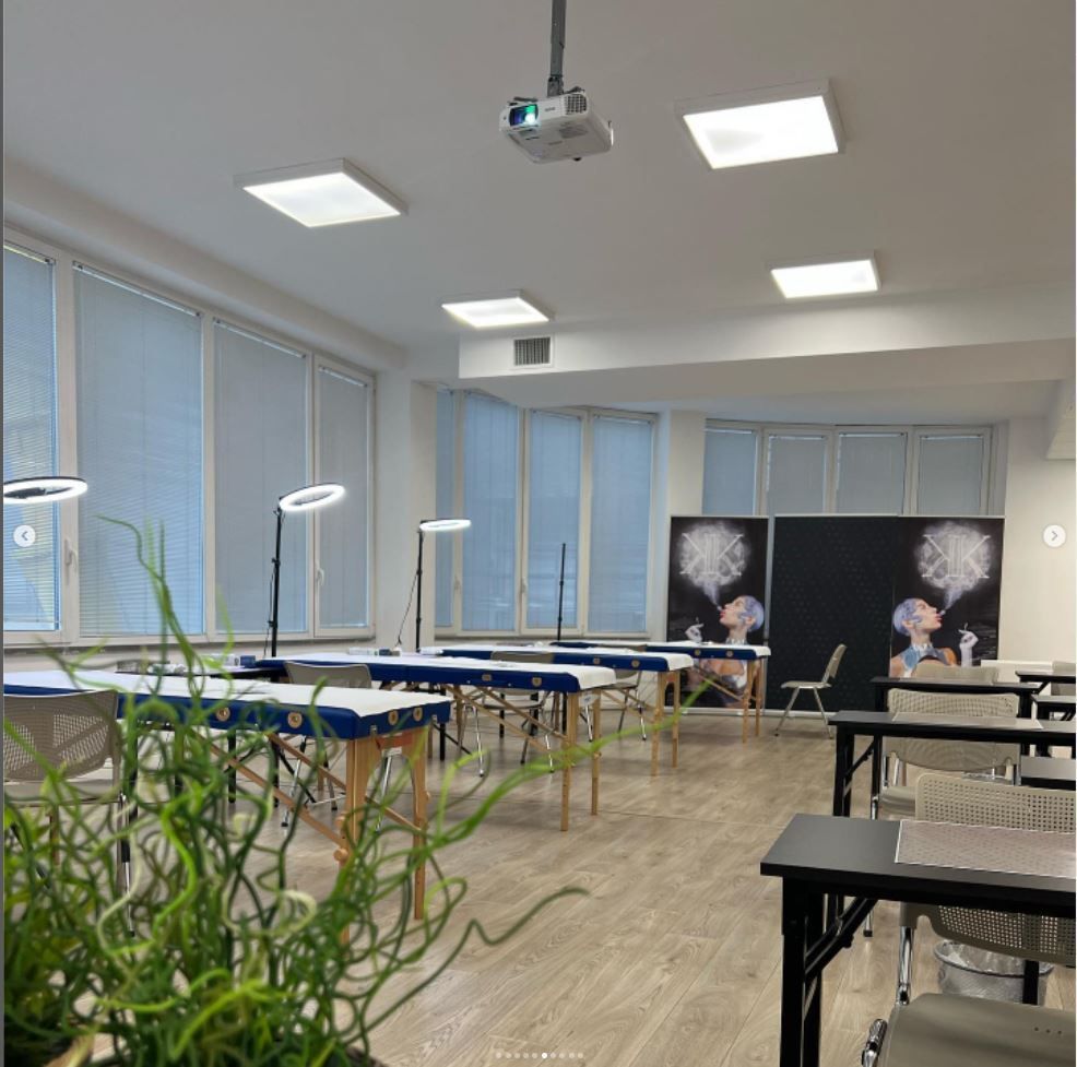 Aula luminosa con tavoli, sedie nere, grandi finestre, luci a soffitto e un proiettore montato sul soffitto.