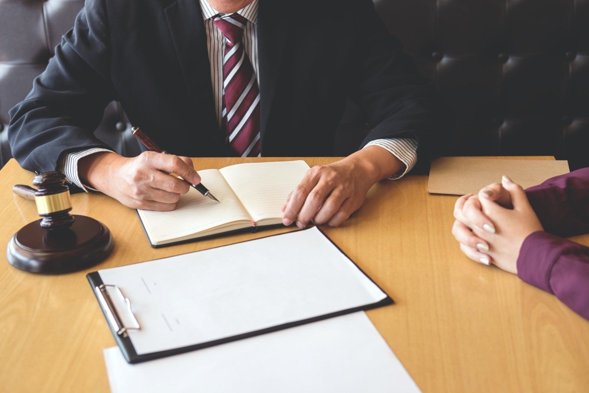A man in a suit and tie is writing in a notebook while sitting at a table with a woman.