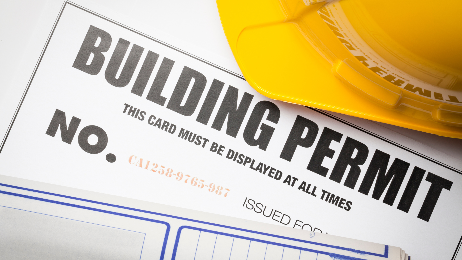 Building permit on blueprints with a yellow tape measure.