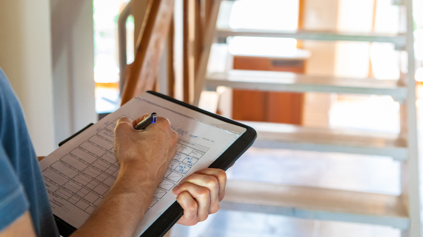 Person writing on a clipboard, standing near a staircase.