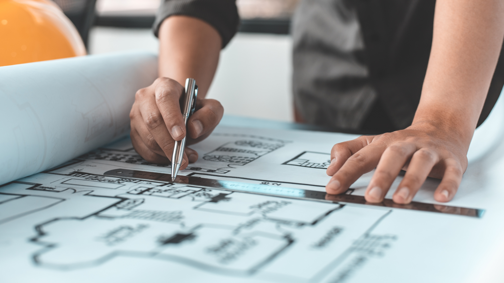 Hands using a pen and ruler to draw on architectural blueprints.