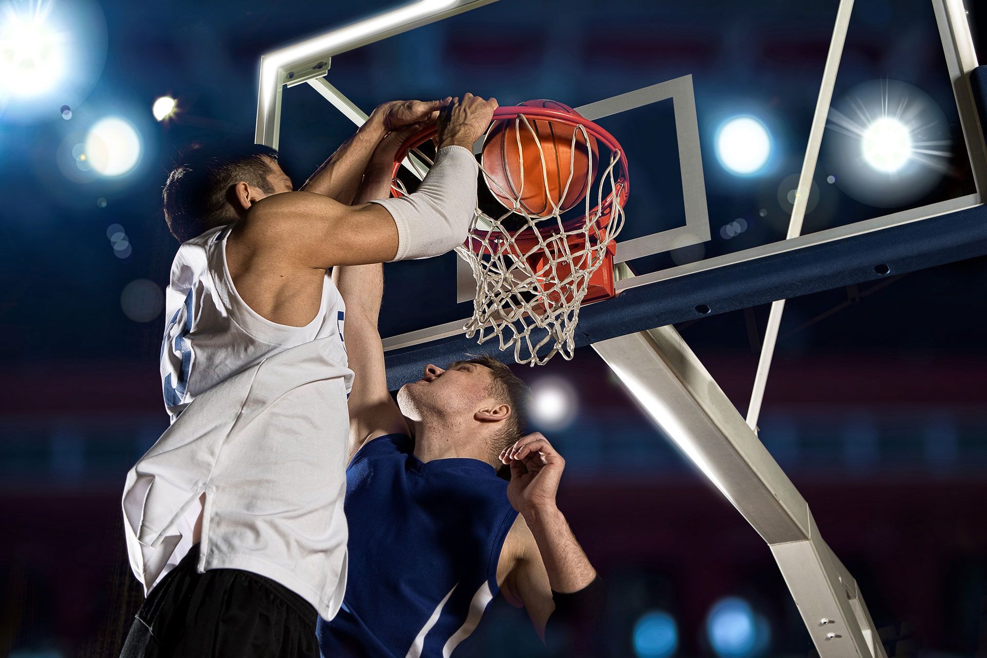Basketball players leaping for a dunk at the hoop under bright arena lights