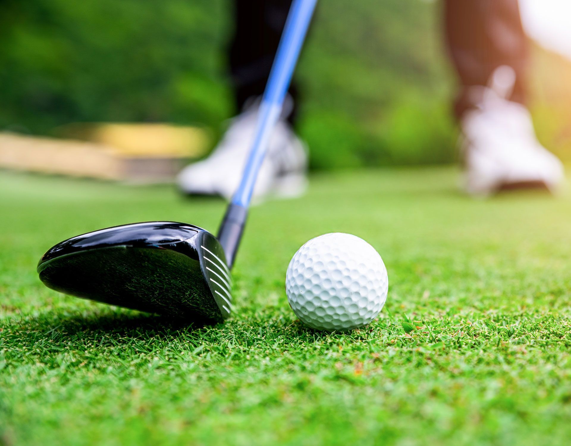 Golf club and ball on green fairway with golfer blurred in the background