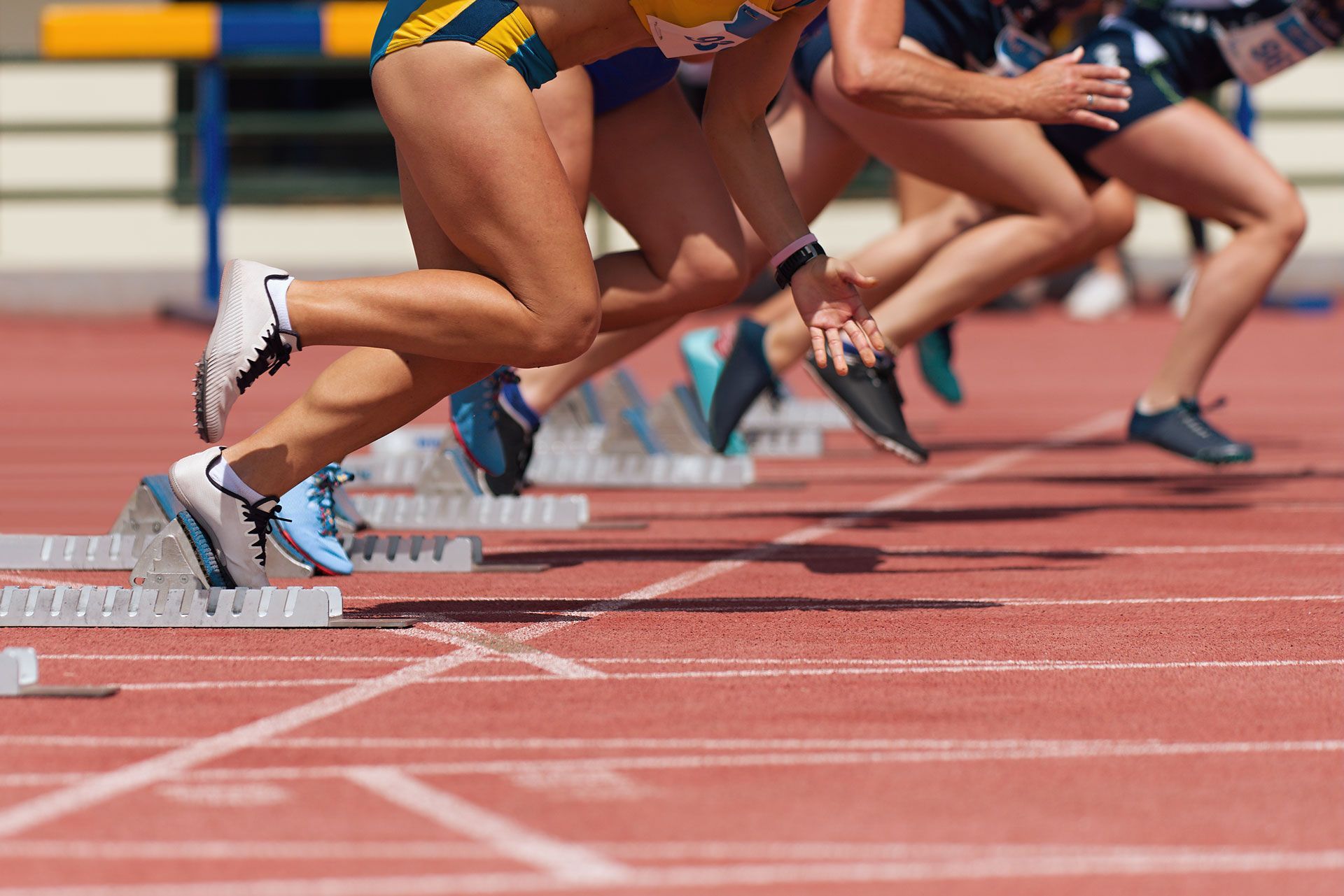 Sprinters launching from starting blocks on a red track, legs blurred in motion