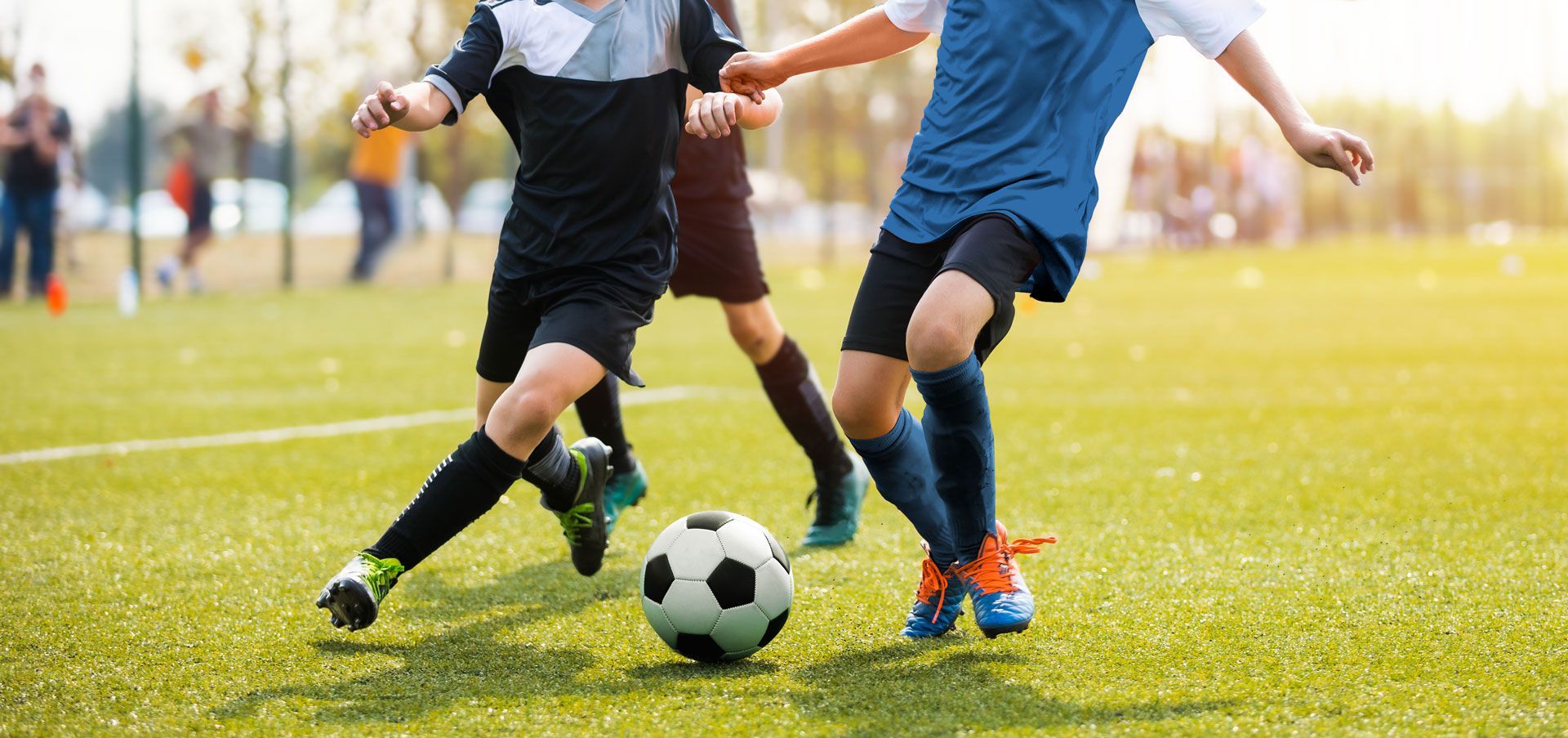 Two soccer players contest a ball on a sunny green field