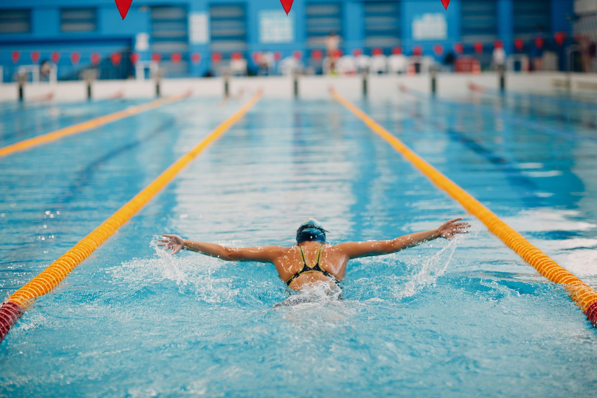 Swimmer performing butterfly stroke in an indoor pool with lane lines and splashing water