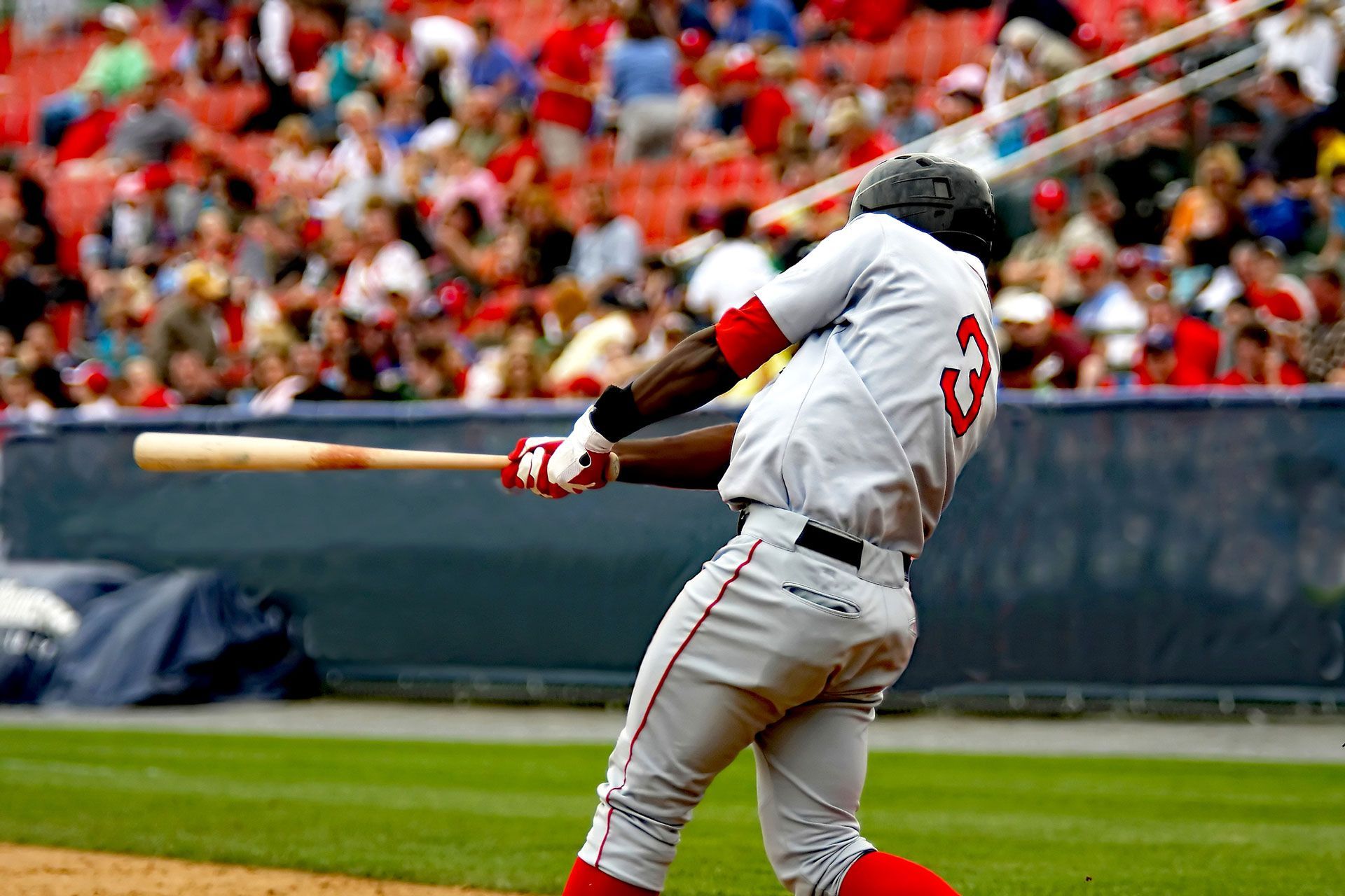 Baseball player in white uniform swinging a bat on the field, with a crowd in the stands.