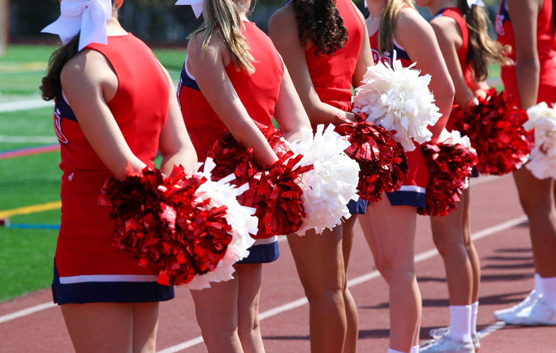 Cheerleaders in red uniforms holding red pom-poms on a track field