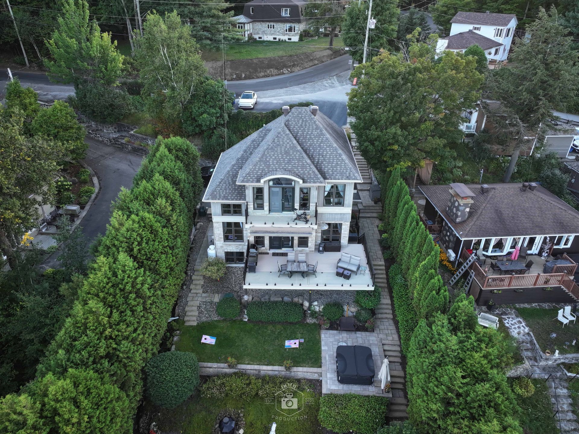 Vue aérienne d'une maison au toit gris avec une grande terrasse, entourée d'arbres et mitoyenne d'une autre maison.