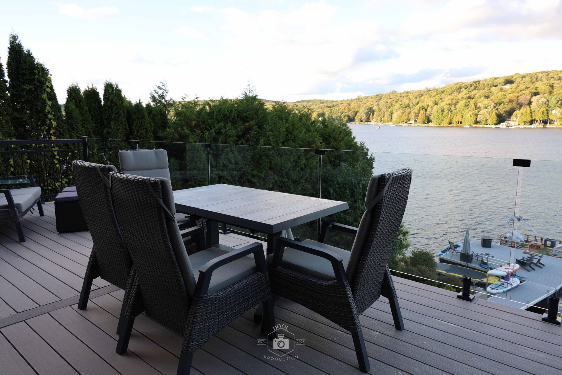 Mobilier de jardin sur une terrasse donnant sur le lac. Des chaises entourent une table. Arbres et eau en arrière-plan.