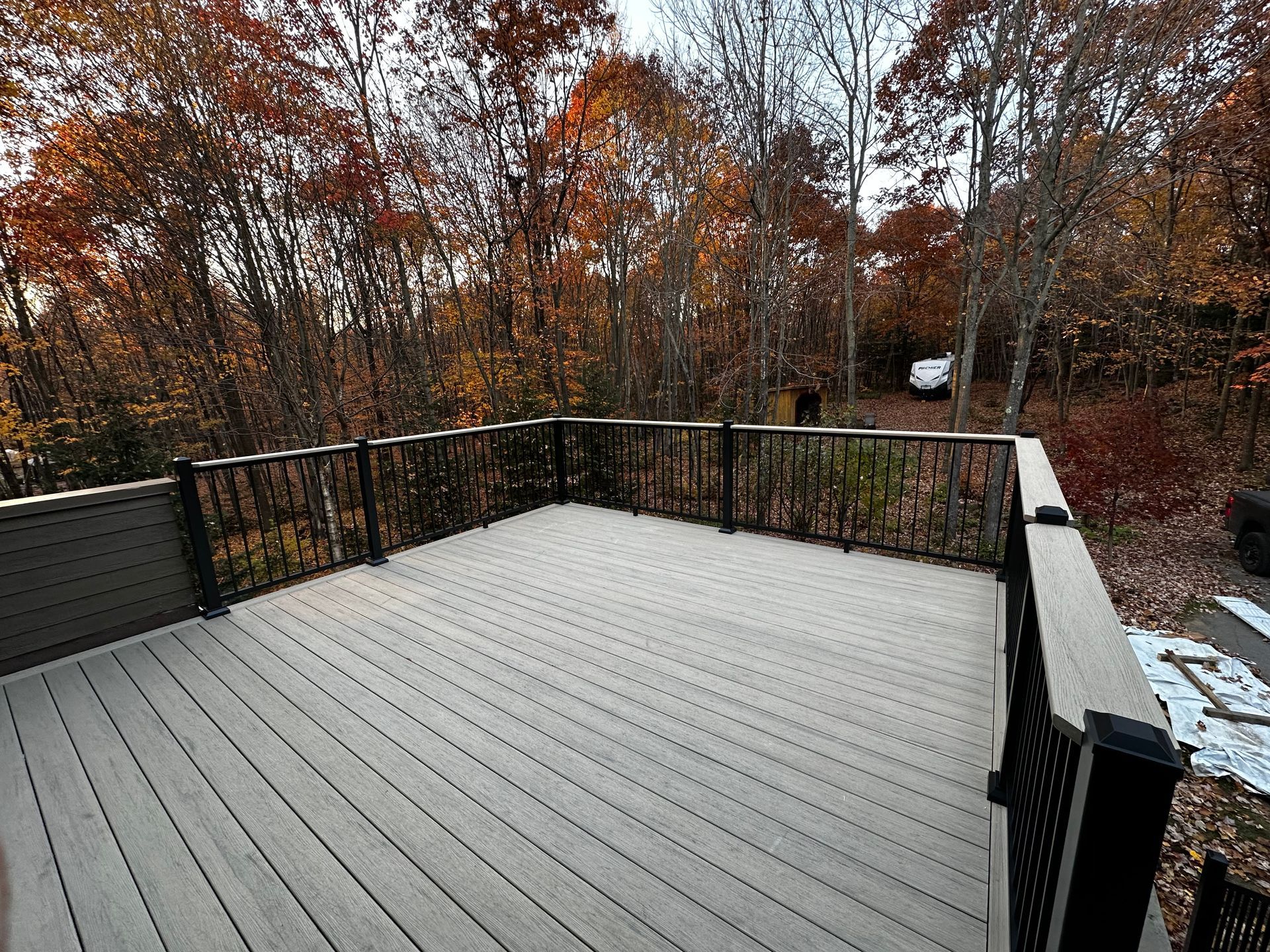 Terrasse en bois avec rambarde noire donnant sur des arbres aux couleurs d'automne.