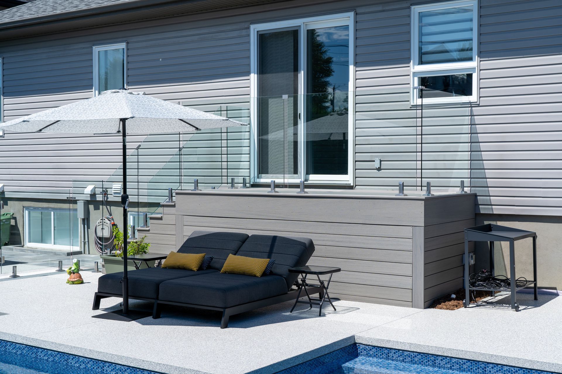 Terrasse extérieure avec piscine, chaises longues et parasol ; balustrade en verre et porte coulissante.