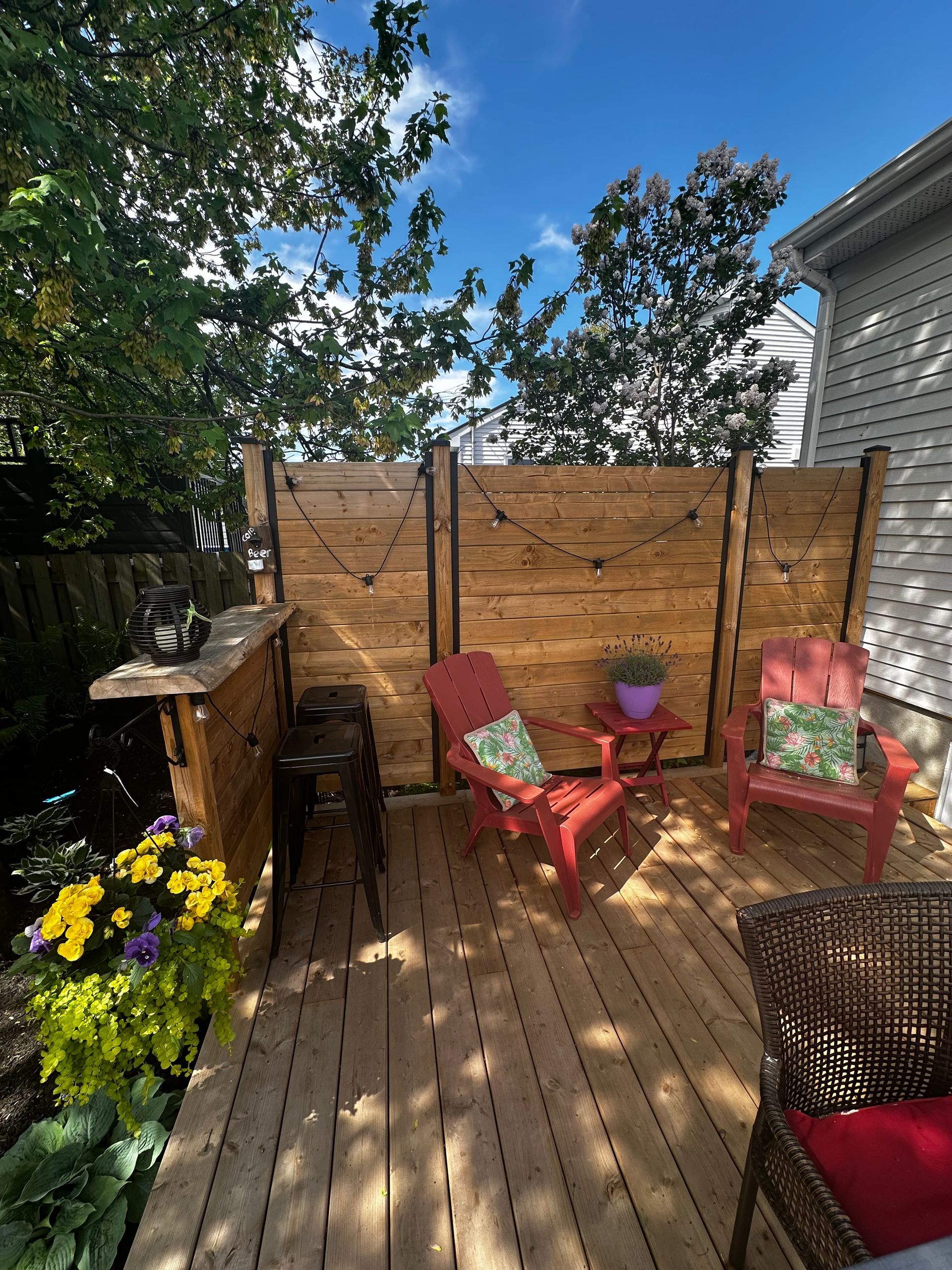 Terrasse extérieure en bois avec sièges, bar et clôture pour plus d'intimité, sous un ciel ensoleillé.