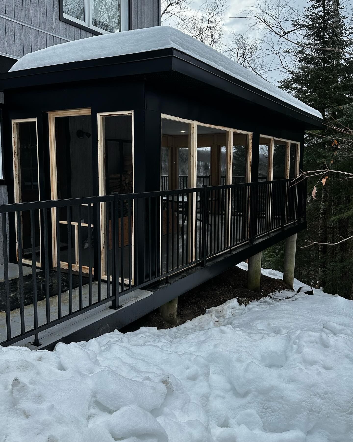 Véranda noire fermée avec rambarde noire et neige, se détachant sur un paysage enneigé.