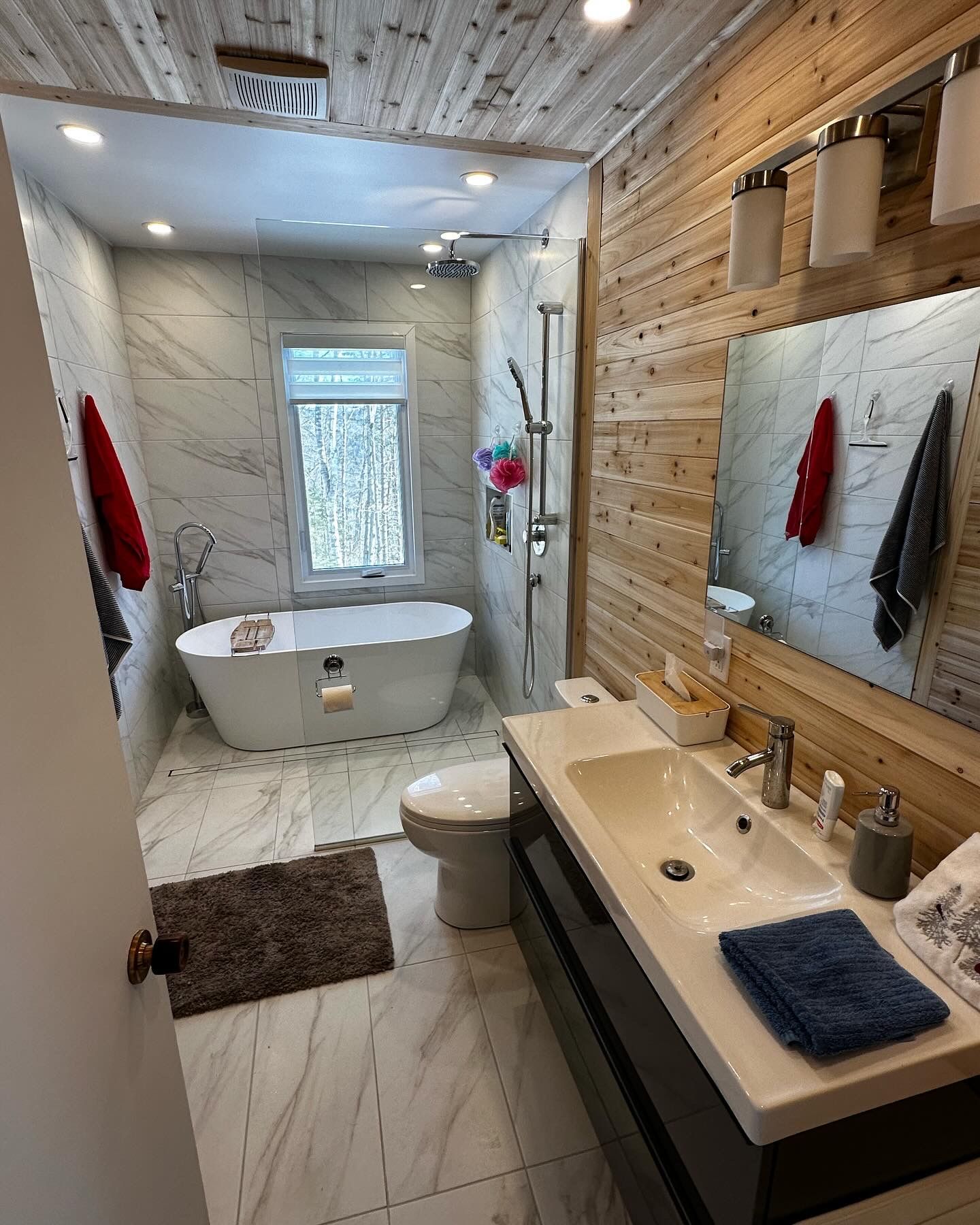 Salle de bains avec baignoire îlot, murs en bois et carrelage en marbre.