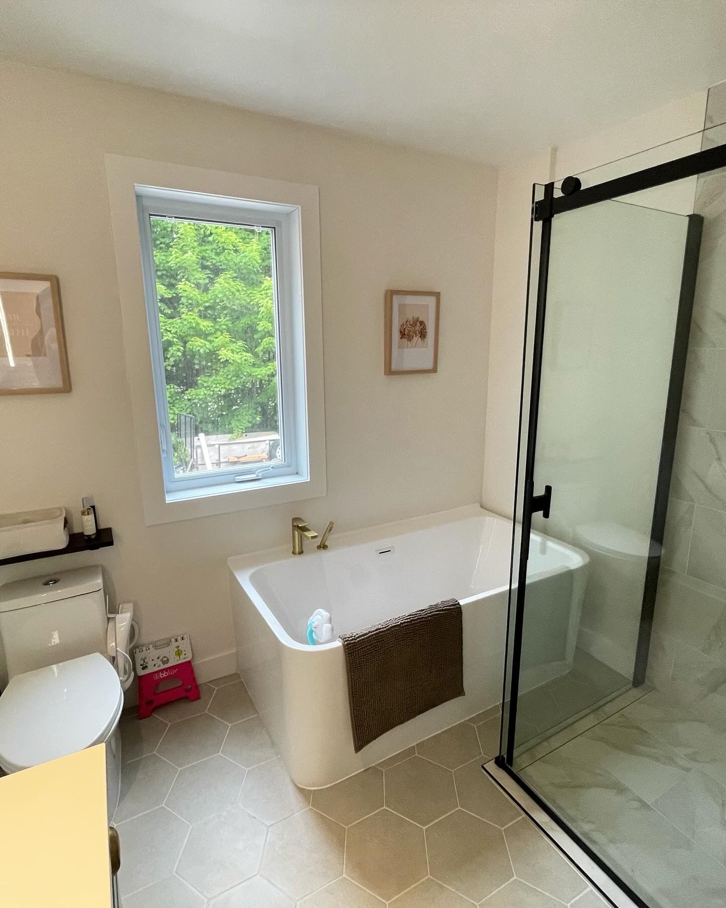 Salle de bains avec baignoire, douche et toilettes. Murs clairs, sol en carrelage hexagonal et fenêtre.