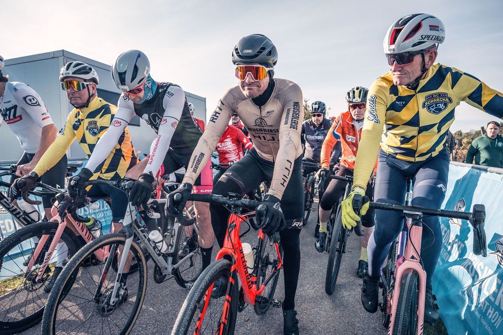 Radfahrer mit Helmen stehen bei verschneitem Start in einer Reihe, sie tragen leuchtende Trikots und fahren Mountainbikes.