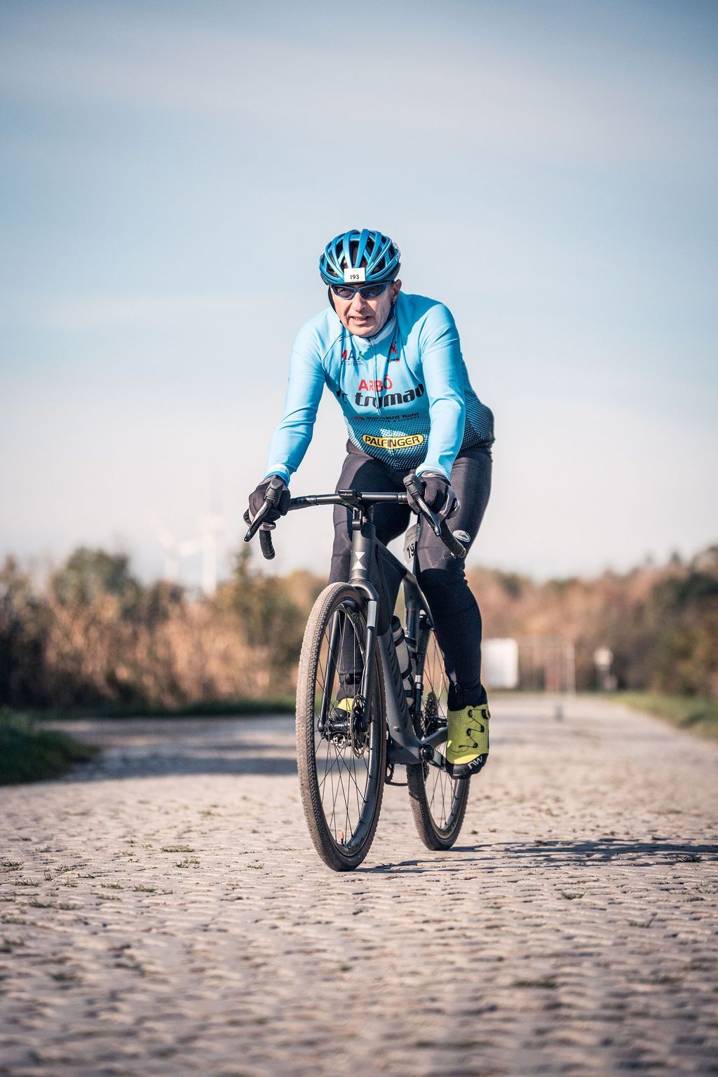 Radfahrer in blauer Ausrüstung fährt auf einem Kopfsteinpflasterweg im Freien