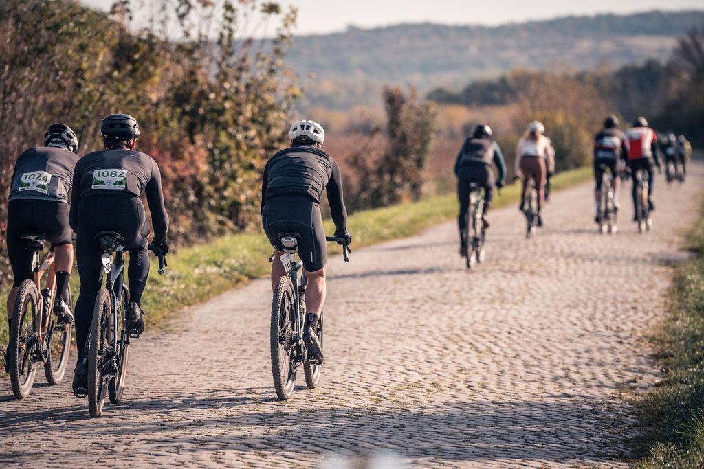 Radfahrer fahren tagsüber auf einer Kopfsteinpflasterstraße durch eine ländliche Landschaft