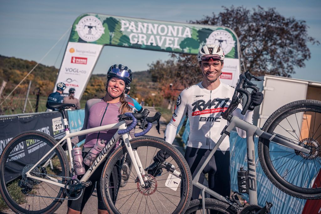 Zwei Radfahrer posieren mit ihren Fahrrädern vor einem Zielbanner des Pannonia Gravel-Events im Freien