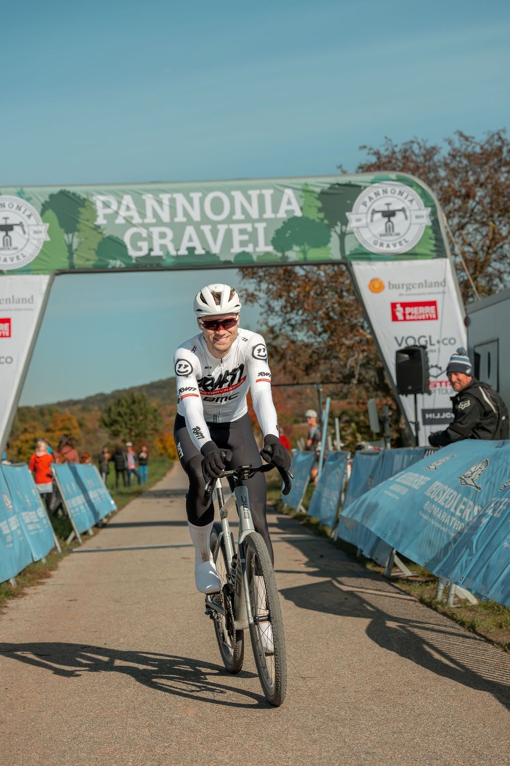 Radfahrer fährt auf einer sonnigen Rennstrecke unter einem „Pannonia Gravel“-Bogen dem Ziel entgegen.