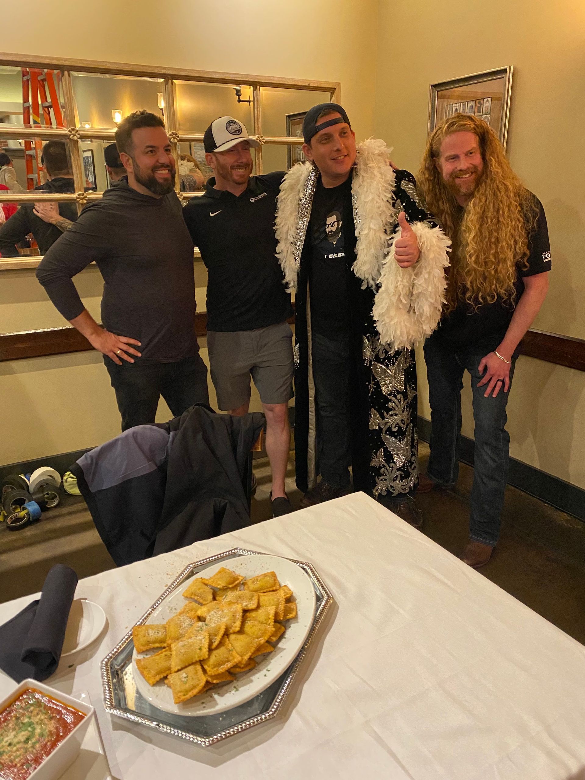 Four friends posing in costumes at a party beside a table with a tray of food.