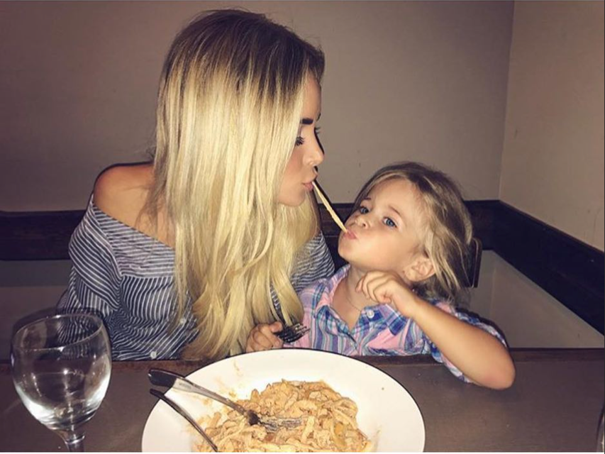Two people sharing spaghetti at a restaurant table, leaning in close and looking at each other.