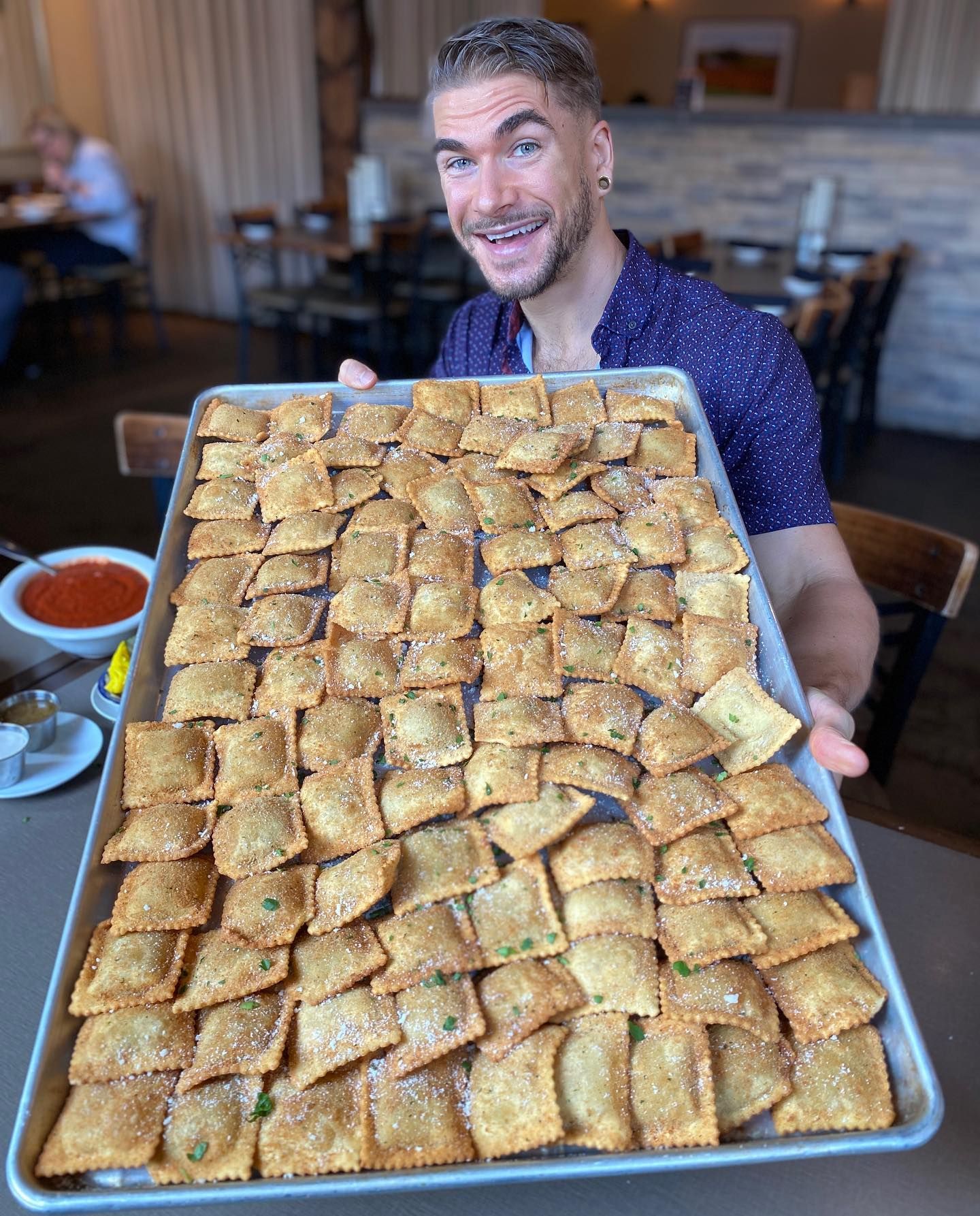 Man holding a large tray of golden baked pastries in a restaurant, smiling at the camera
