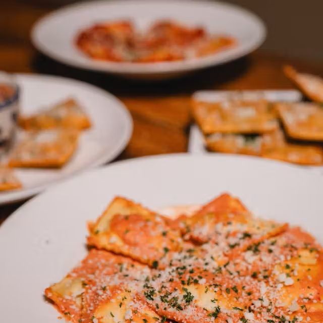 Two saucy ravioli on a white plate, topped with grated cheese and herbs
