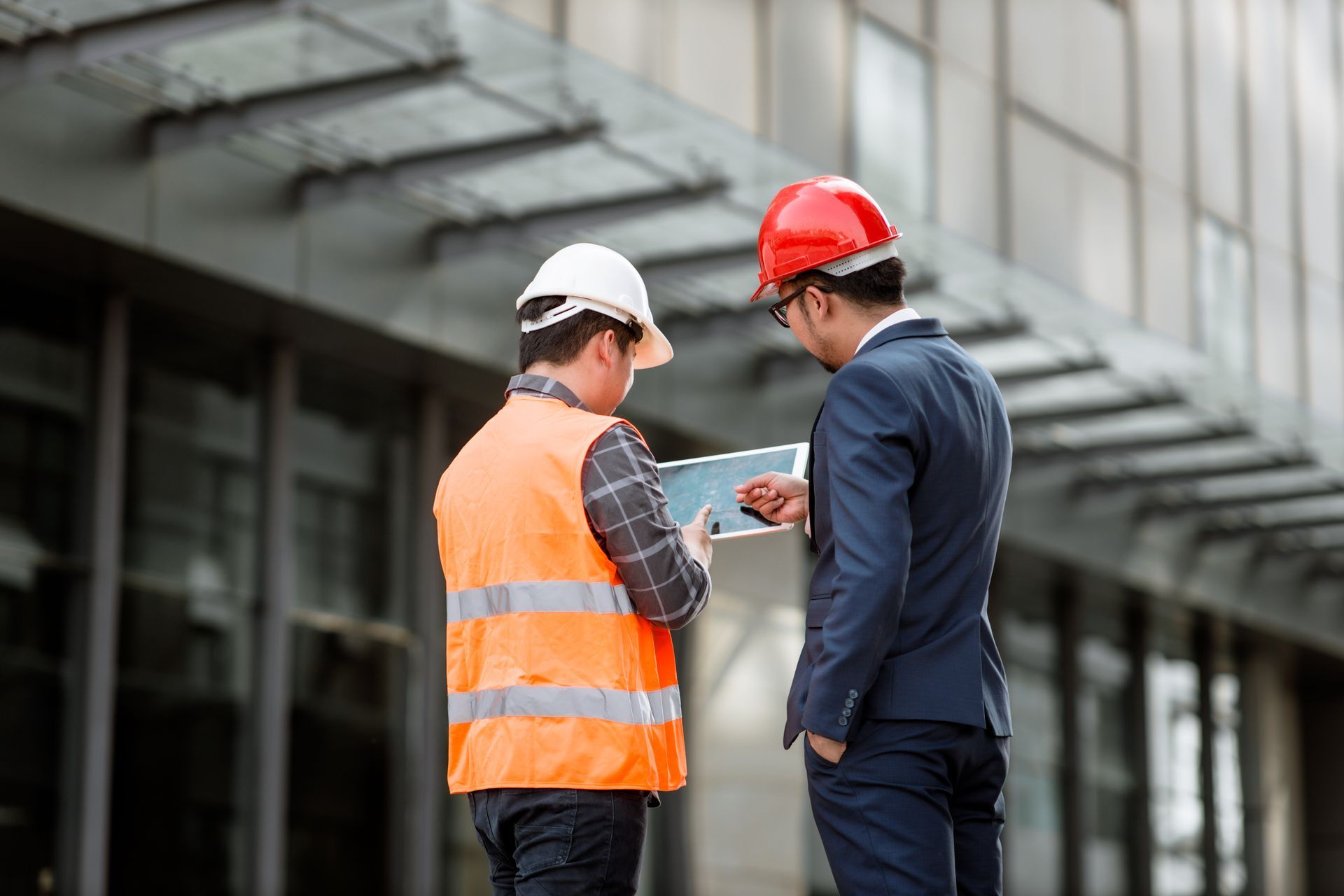Two people in hard hats review plans outside a modern building.