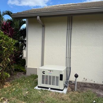 Outdoor HVAC unit beside a beige house wall with two vertical pipes and surrounding grass and plants