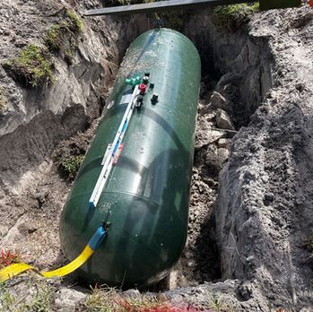Green cylindrical pipeline section in a dirt trench, with workers and tools attached on top.