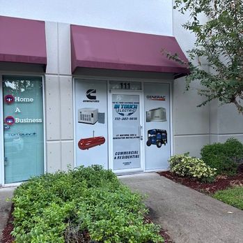 Storefront with maroon awning, glass doors, and business decals beside shrubs and a sidewalk.