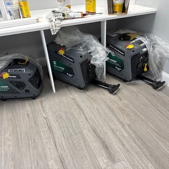Three portable power generators under a shelf in a store, wrapped in plastic.