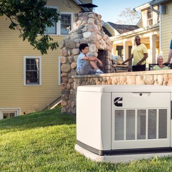 People relaxing on a stone patio beside a white outdoor HVAC unit and yellow house
