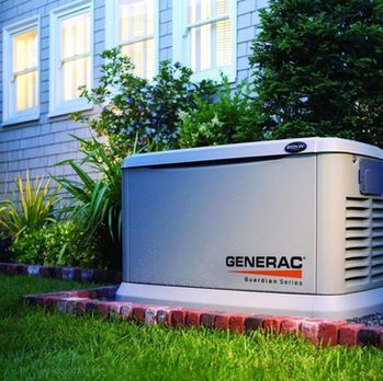 Generac standby generator beside a house, set on a red concrete pad amid green landscaping