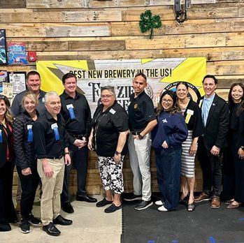 Group of people posing indoors in front of a yellow brewery banner and wood wall