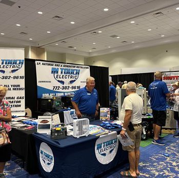 Booth for THURIC Electric at a trade show, with staff behind a table and a customer browsing flyers