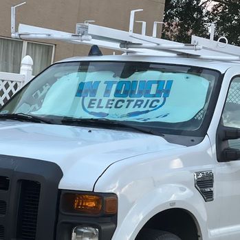 White utility truck with a blue “TOUCH ELECTRIC” windshield sign parked outdoors.