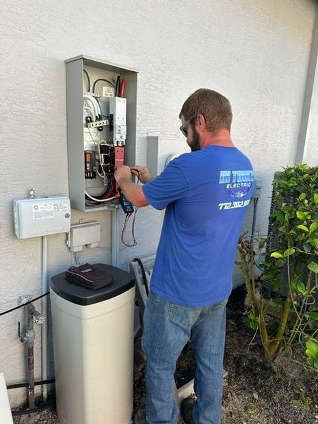 Technician testing an outdoor electrical panel beside a beige building and air conditioning unit