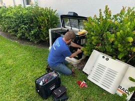 Technician kneeling beside outdoor HVAC unit, repairing equipment near a hedge on a lawn.