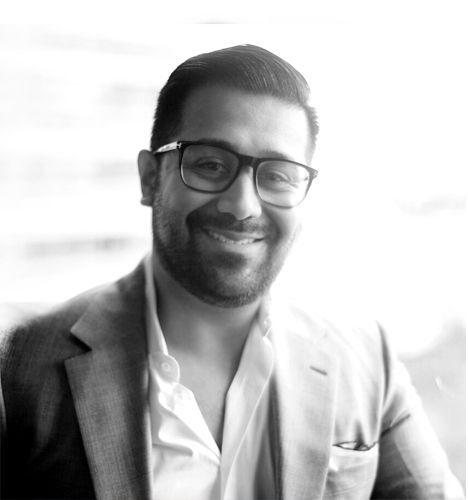 A man wearing glasses and a suit is smiling in a black and white photo.